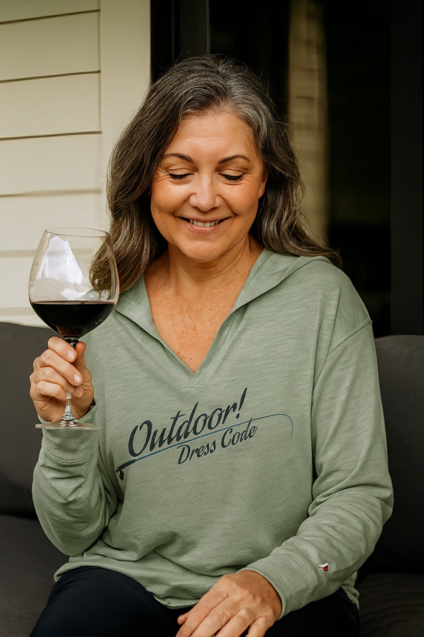 Woman wearing a green 'Outdoor Dress Code' shirt, holding a glass of red wine.