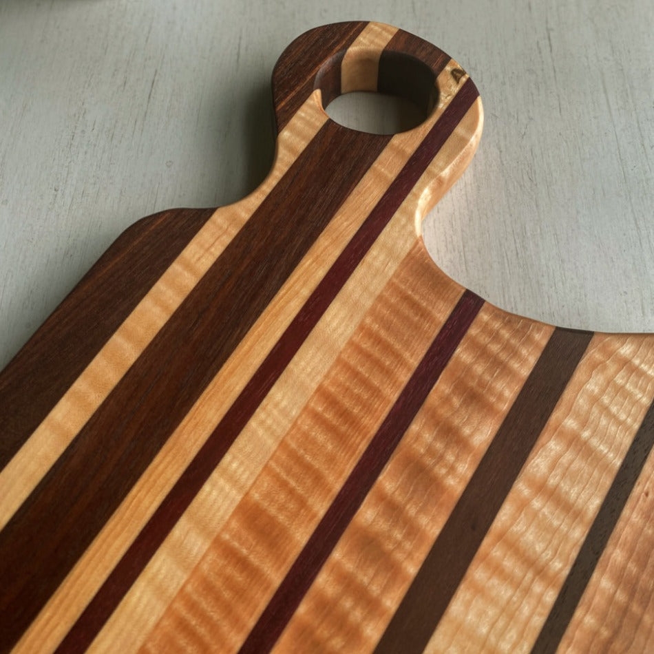 This handcrafted Charcuterie Board is created with Curly Birch, Walnut and Purple Heart with a Millie's All-Purpose Penetrating Tung Oil finish. It measures 17