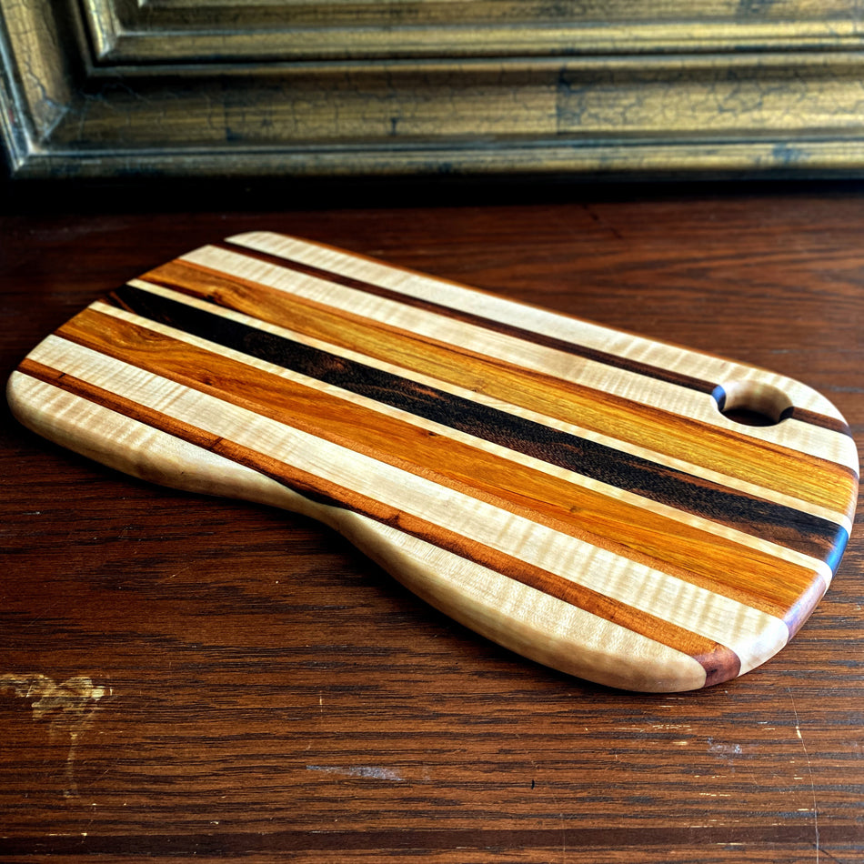 This charcuterie board is crafted with three types of wood: Carnary, Tiger Maple, and Goncalo Alves. It makes a stylish presentation for last-minute gatherings and has been expertly seasoned. It is sealed with Sutherland Welles Ltd.® Millie's All-Purpose Penetrating Tung Oil.