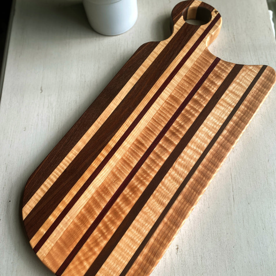 This handcrafted Charcuterie Board is created with Curly Birch, Walnut and Purple Heart with a Millie's All-Purpose Penetrating Tung Oil finish. It measures 17