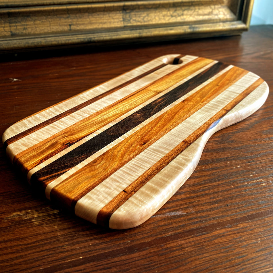 This charcuterie board is crafted with three types of wood: Carnary, Tiger Maple, and Goncalo Alves. It makes a stylish presentation for last-minute gatherings and has been expertly seasoned. It is sealed with Sutherland Welles Ltd.® Millie's All-Purpose Penetrating Tung Oil.