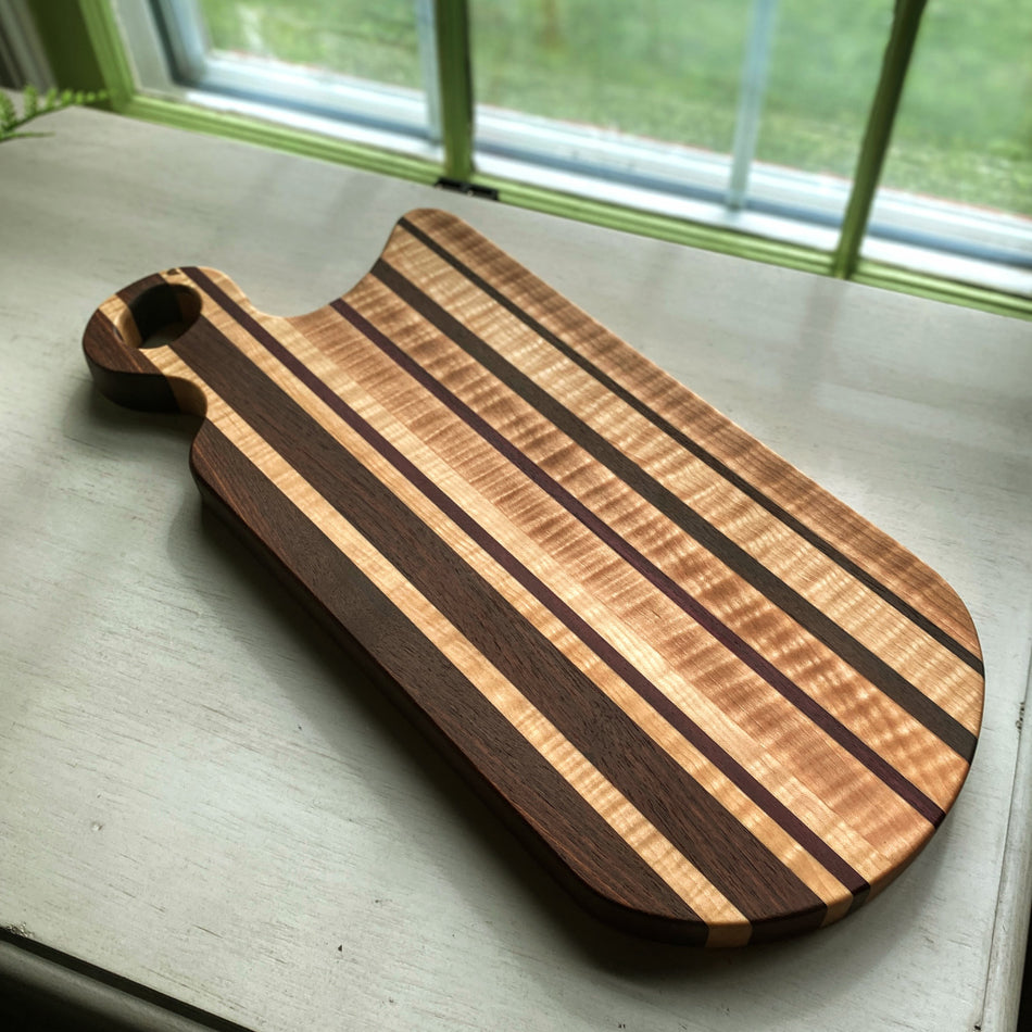 This handcrafted Charcuterie Board is created with Curly Birch, Walnut and Purple Heart with a Millie's All-Purpose Penetrating Tung Oil finish. It measures 17