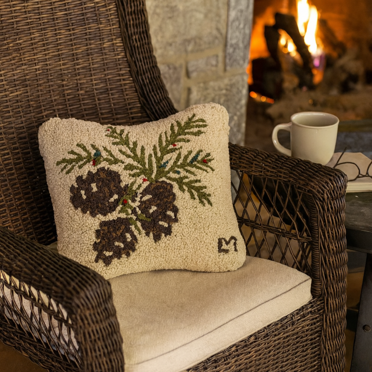Decorative pillow with pinecones and greenery on a wicker chair in front of a fireplace.