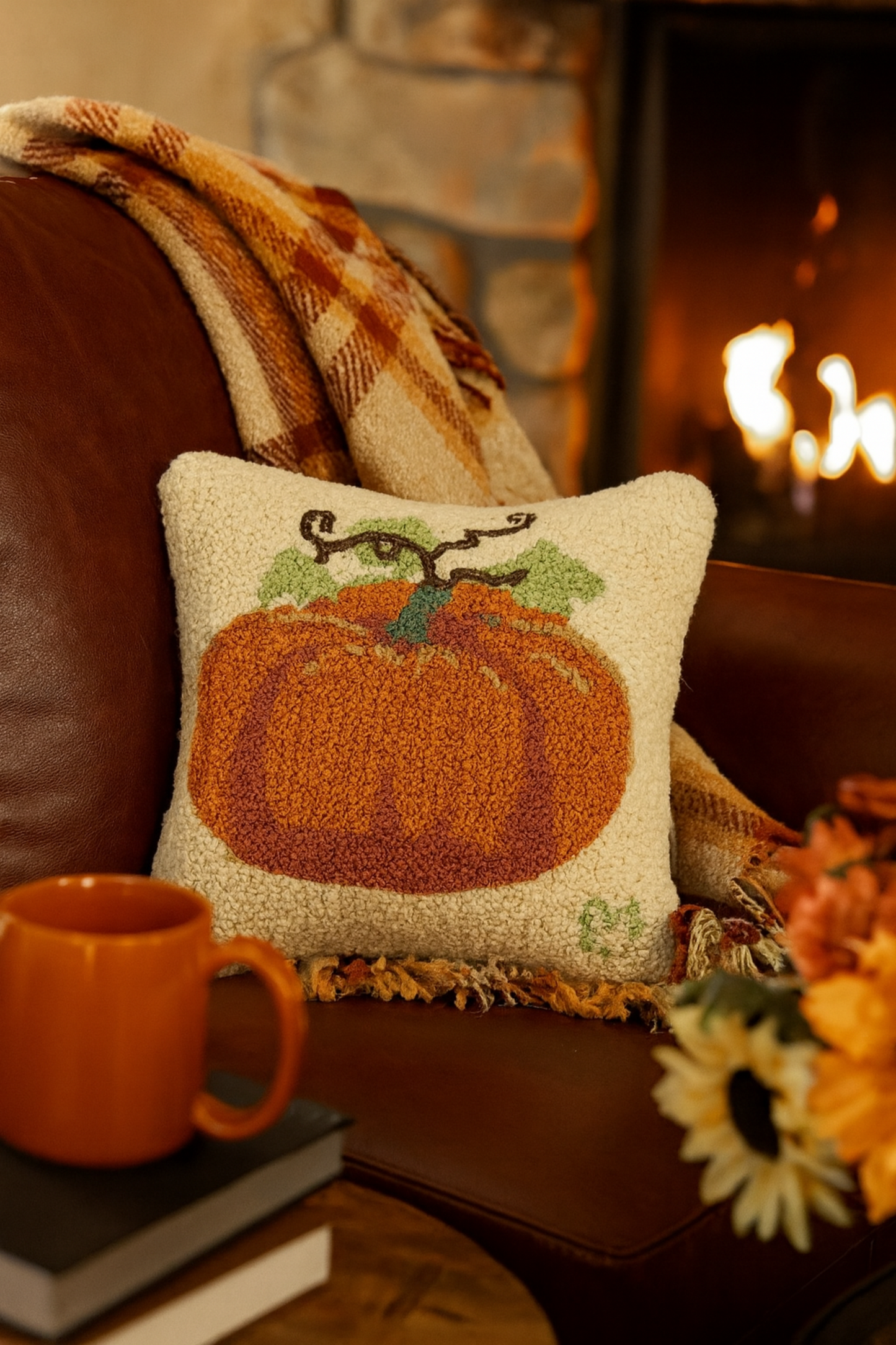 Decorative pillow with a pumpkin design on a couch next to a mug and books, with a fireplace in the background.