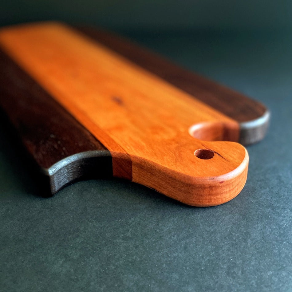 The Handcrafted Charcuterie Board is crafted from Gummy Cherry, Cherry and Walnut measuring 18 x 8 x 1. This combination of woods offers remarkable depth. It is then seasoned with Milie's Tung Oil.