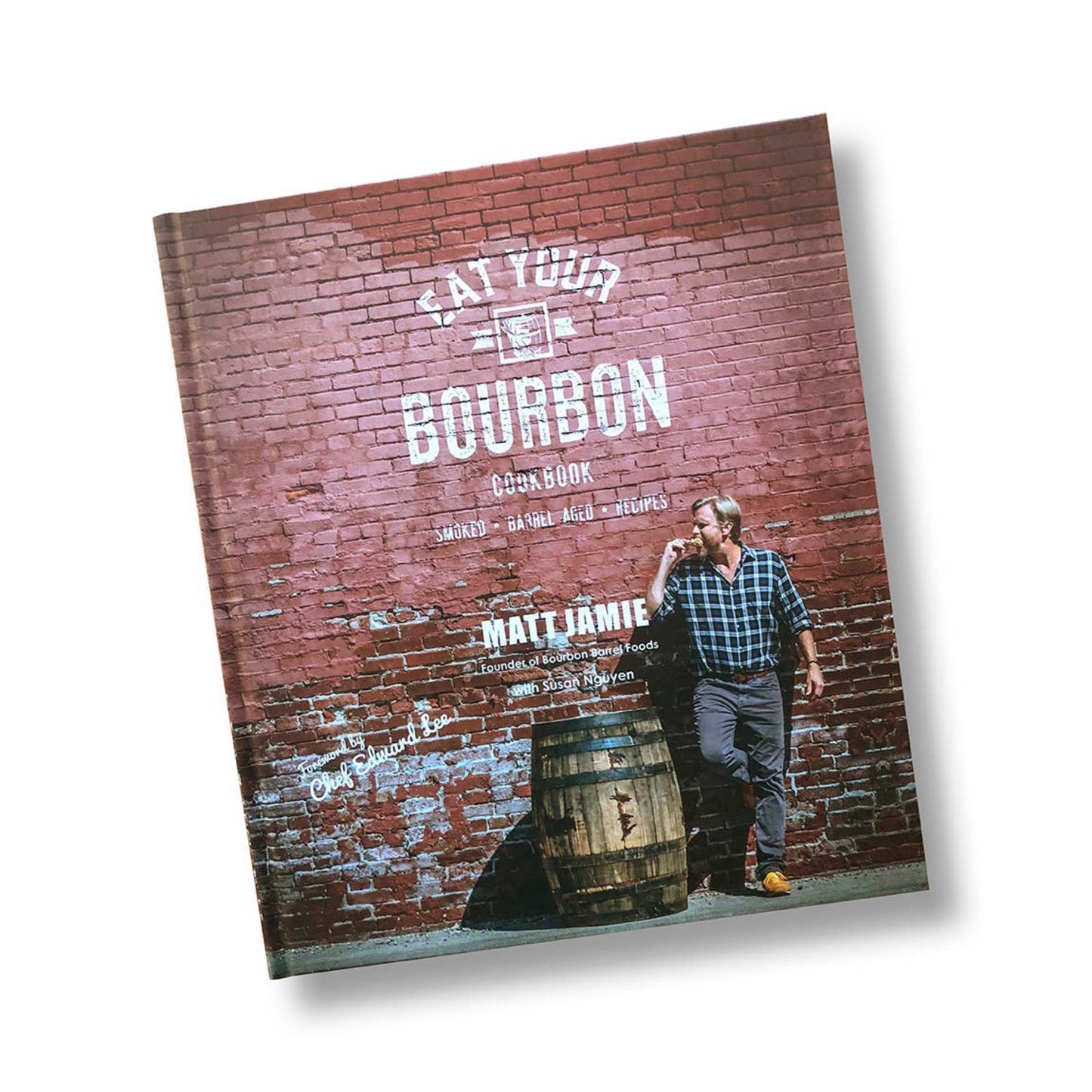 Book titled 'Make Your Own Bourbon' with a person standing next to a barrel against a brick wall.