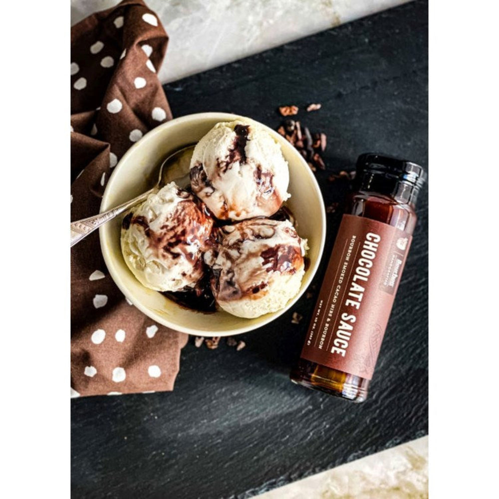 
                  
                    Bourbon Smoked Cacao Nibs infuse this signature Chocolate Sauce with a delightful texture. It’s a harmonious blend of creaminess and crunchiness, complemented by its rich and bittersweet flavor. Indulge in this decadent treat by spooning it over ice cream or drizzling it on your favorite fruits.
                  
                