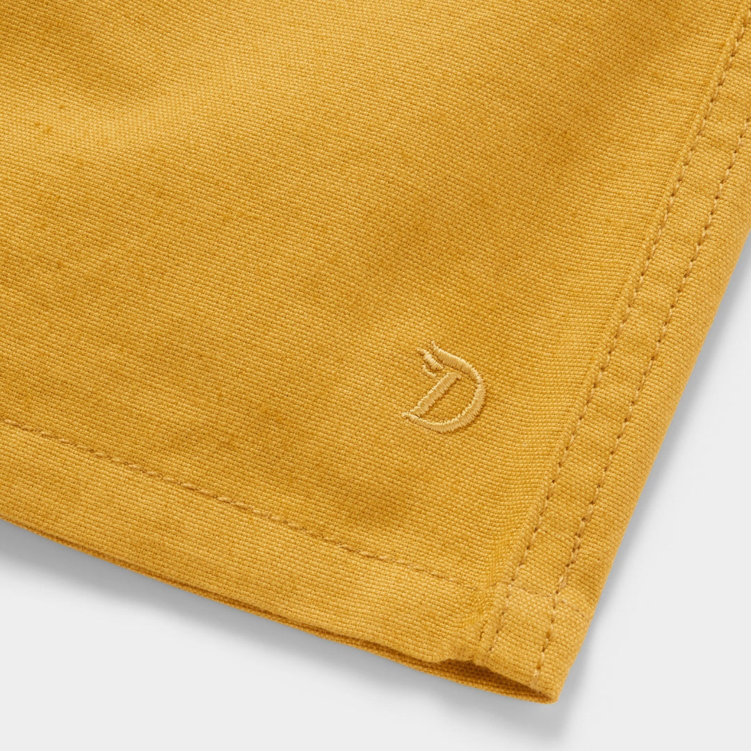 Close-up of a mustard yellow fabric with a brand logo on a white background