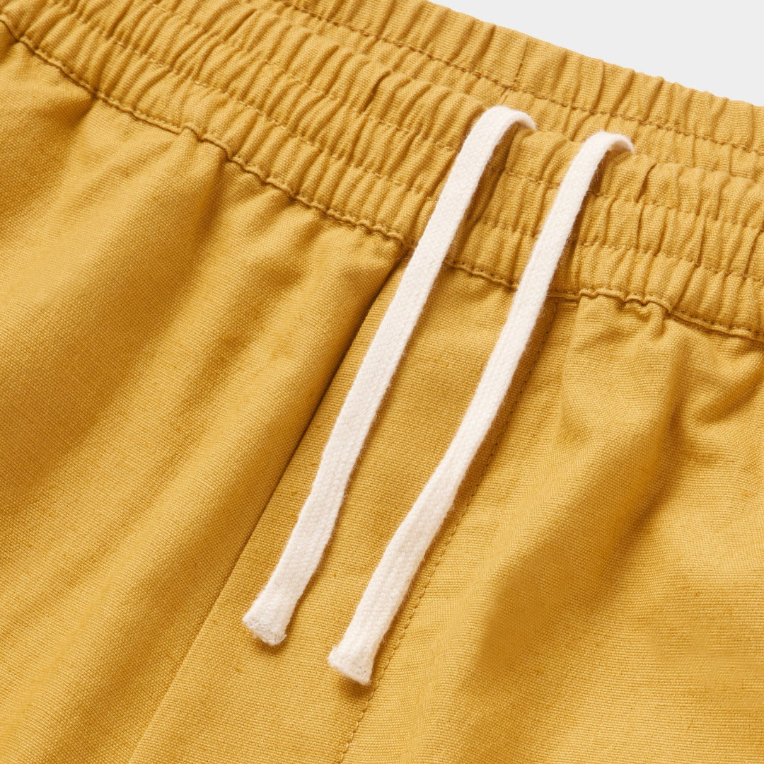 Close-up of mustard yellow shorts with white drawstring on a light gray background