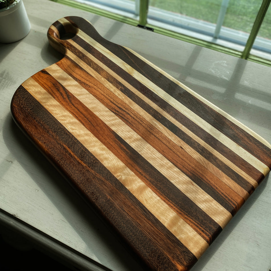 
                  
                    Composed of Tiger Heart, Goncalo Alves and Black Limba, the 19" long, 10" wide, Handcrafted Charcuterie Board is a stunning 1" thick spectacle of contrast and color.
                  
                