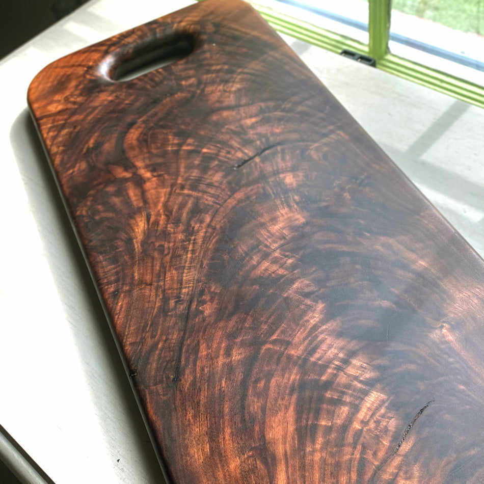 This Handcrafted Charcuterie Board is fashioned from Highly Figured Walnut wood from the Northeastern States. Its generously sized design, measuring 22" Long, 9" wide, and " thick, and weighing nearly 15 pounds, creates an impressive centerpiece for any gathering.