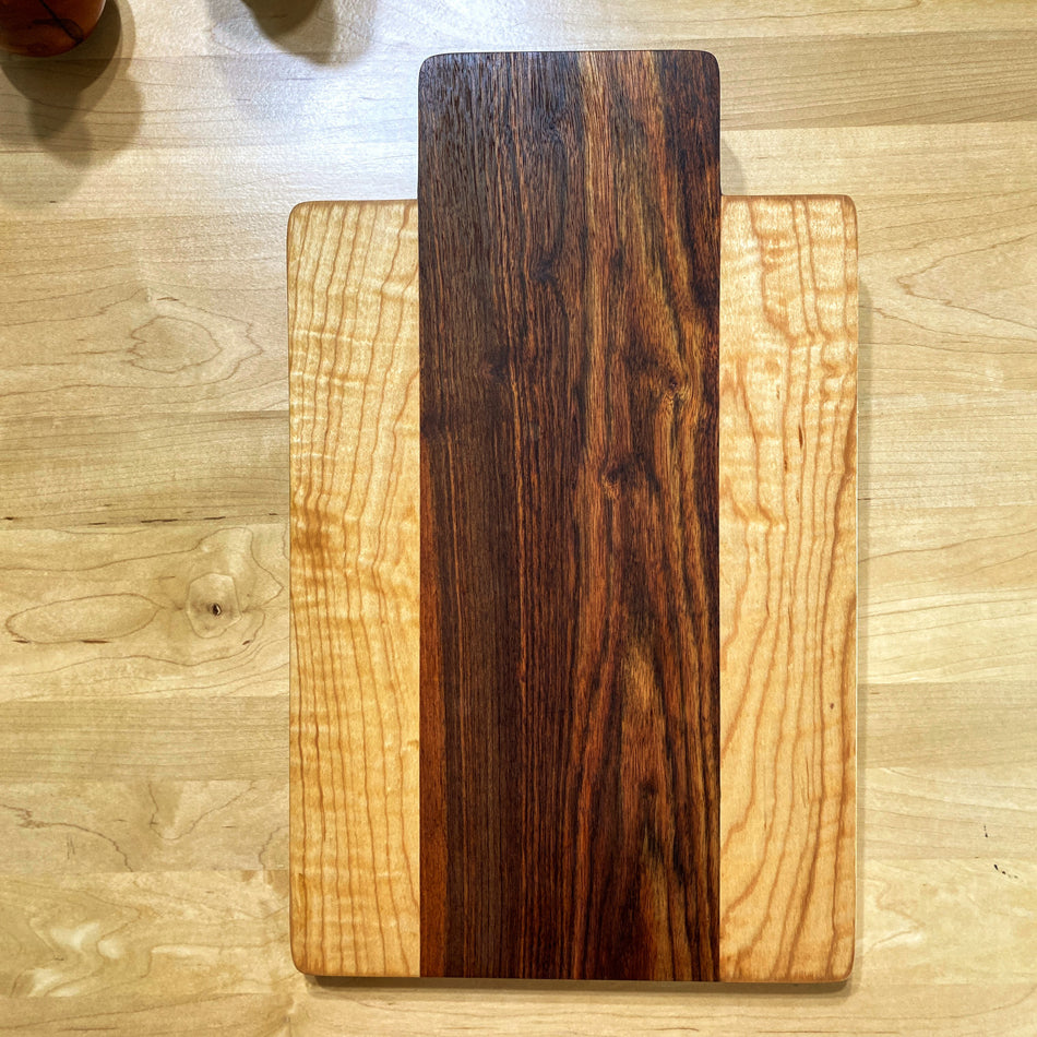 This remarkable Charcuterie Board is handmade with Caribbean Rosewood and Curly Birchwood. These exquisite woods create a stunning color combination, perfect for patio evenings with cocktails and sushi. This board is double-sided and offers an ideal size for crafting delightful charcuterie spreads.