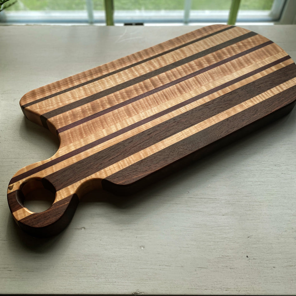 This handcrafted Charcuterie Board is created with Curly Birch, Walnut and Purple Heart with a Millie's All-Purpose Penetrating Tung Oil finish. It measures 17