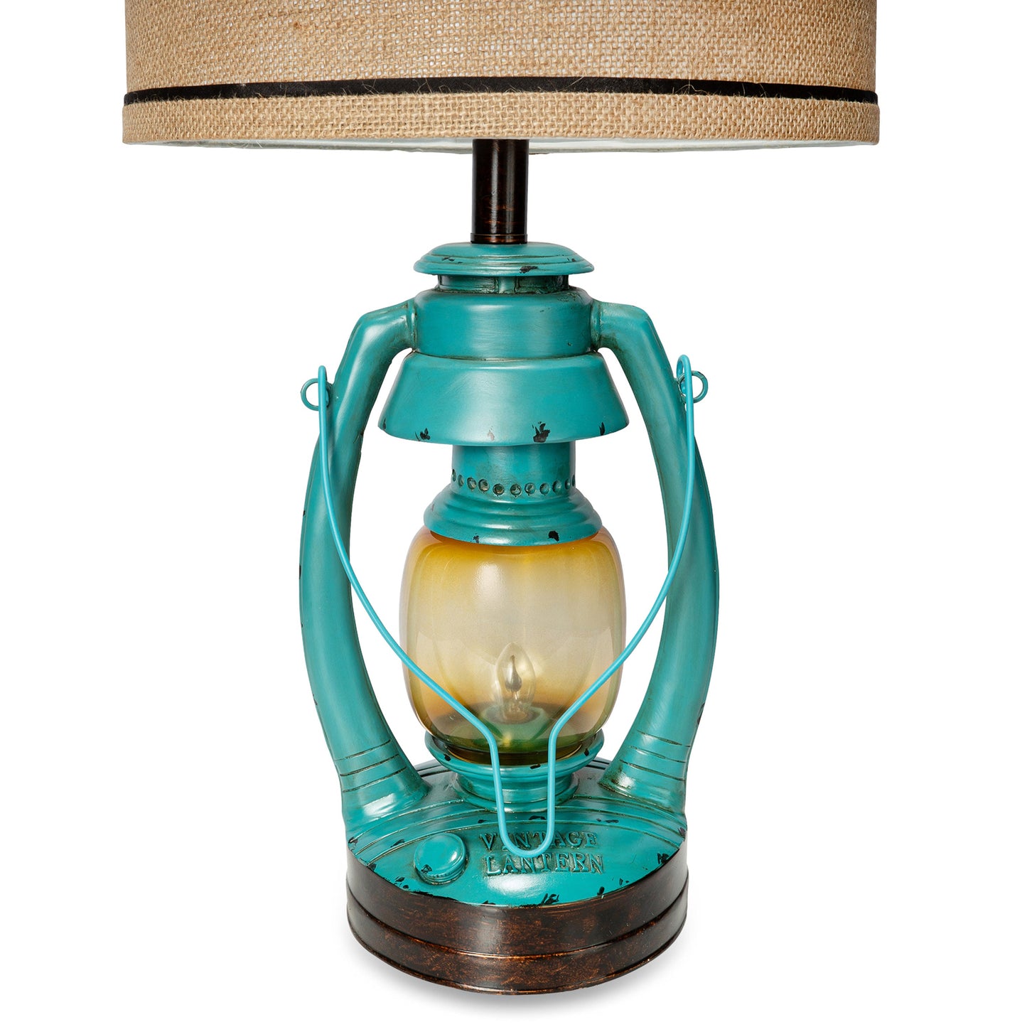 A vintage-style table lamp featuring a distressed turquoise metal lantern base with a warm amber glass center and a beige burlap lampshade with a black band.