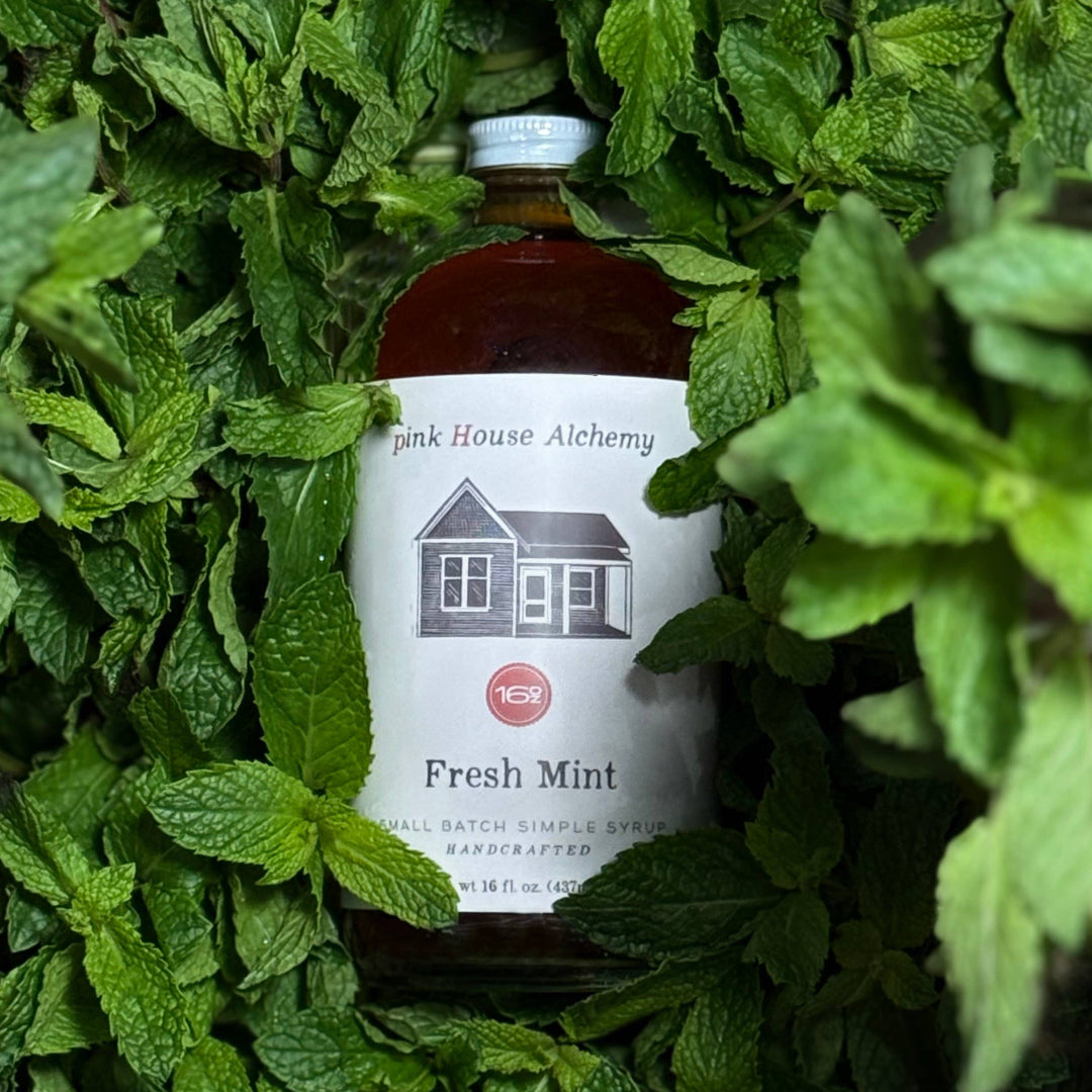 Bottle of 'Pink House Alchemy' Fresh Mint syrup surrounded by mint leaves