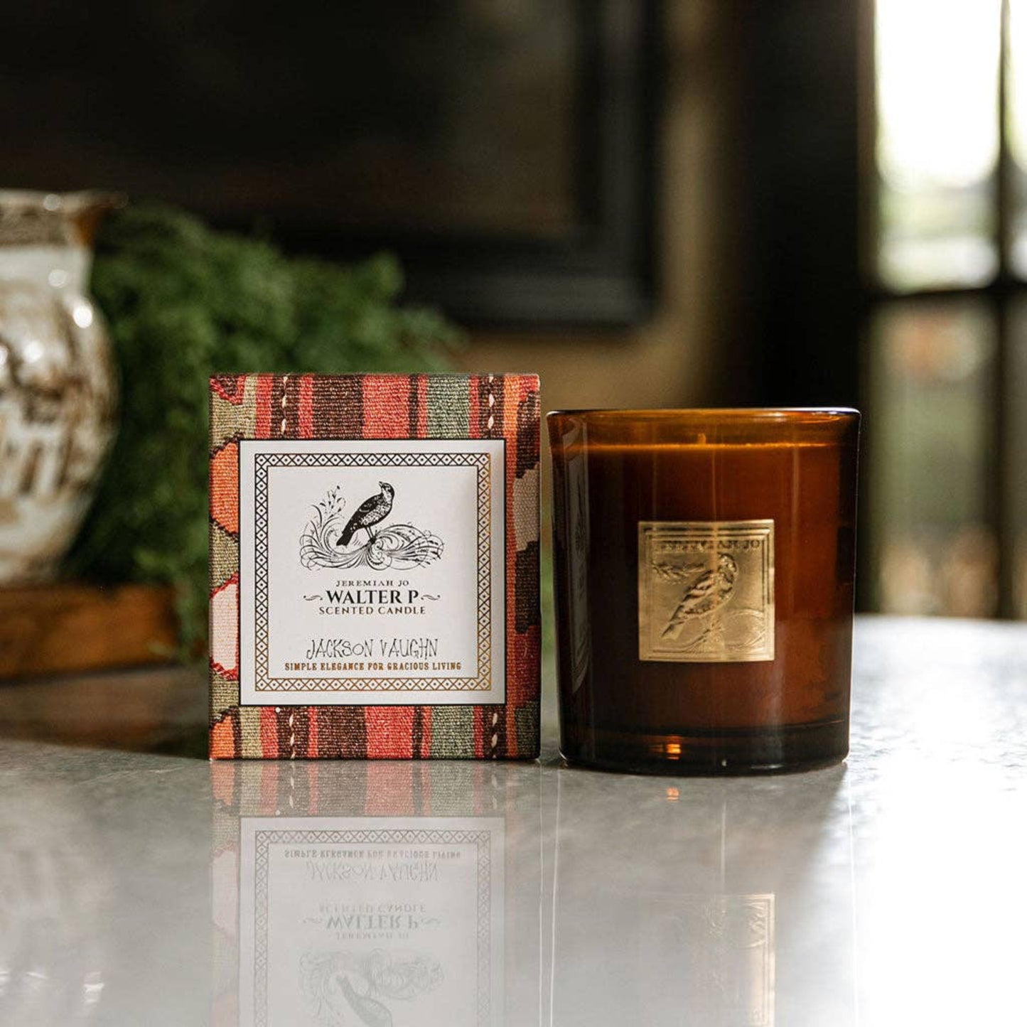 Amber glass candle with gold label beside patterned gift box reading “Walter P. – Jeremiah Jo – Jackson Vaughn,” styled on a marble surface with warm, vintage décor.